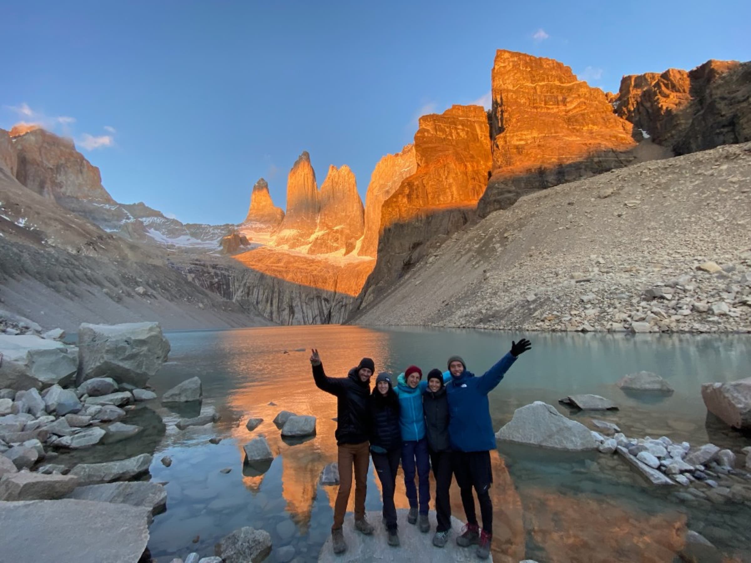 Group of hikers waving beside the lagoon below the towers lit orange at sunrise, Torres del Paine